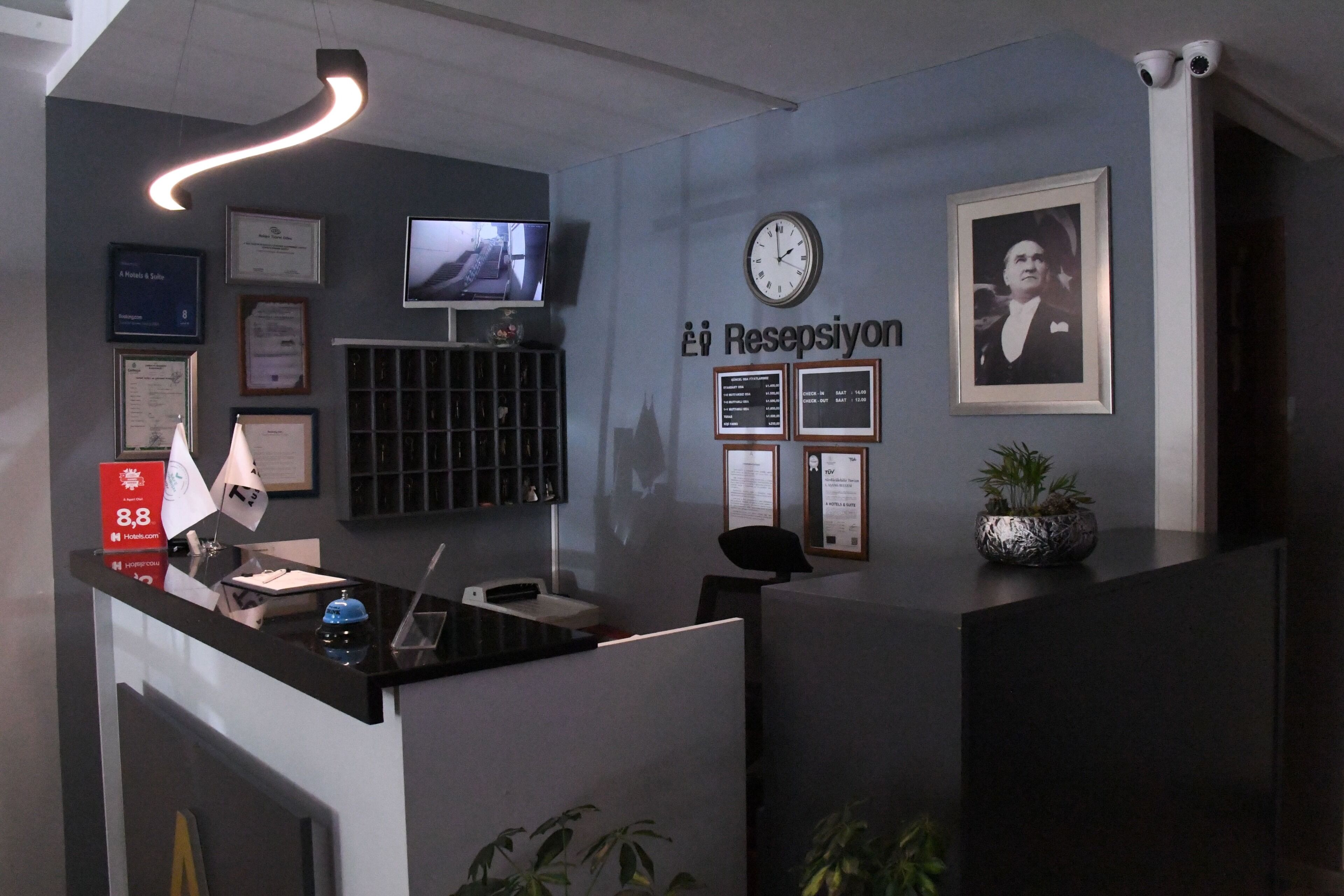 Een hotel receptiebalie met een klok, ingekaderde certificaten, een televisie en een potplant.