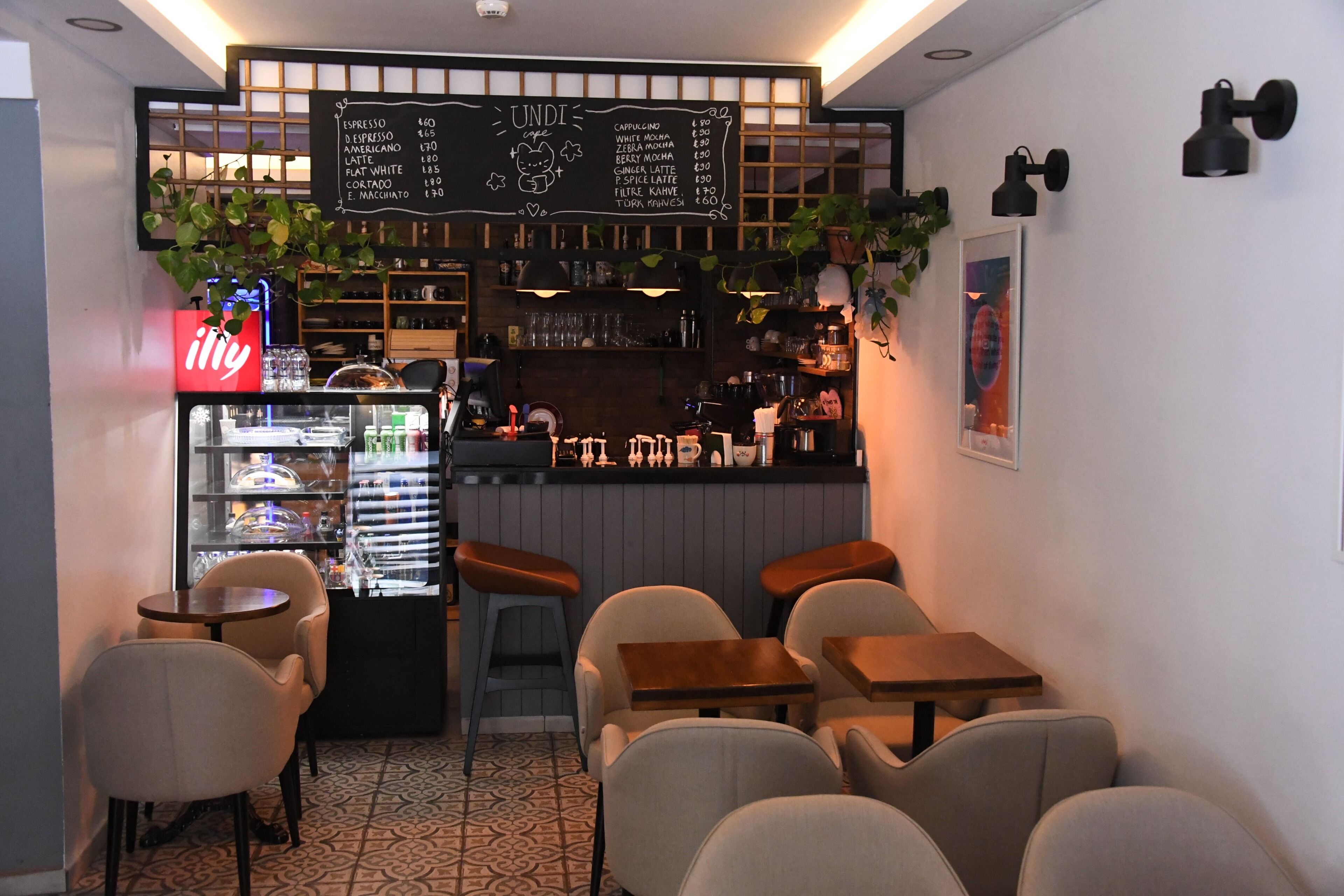 Interior de una cafetería con una pizarra de menú, zona de estar y dispensador de bebidas.