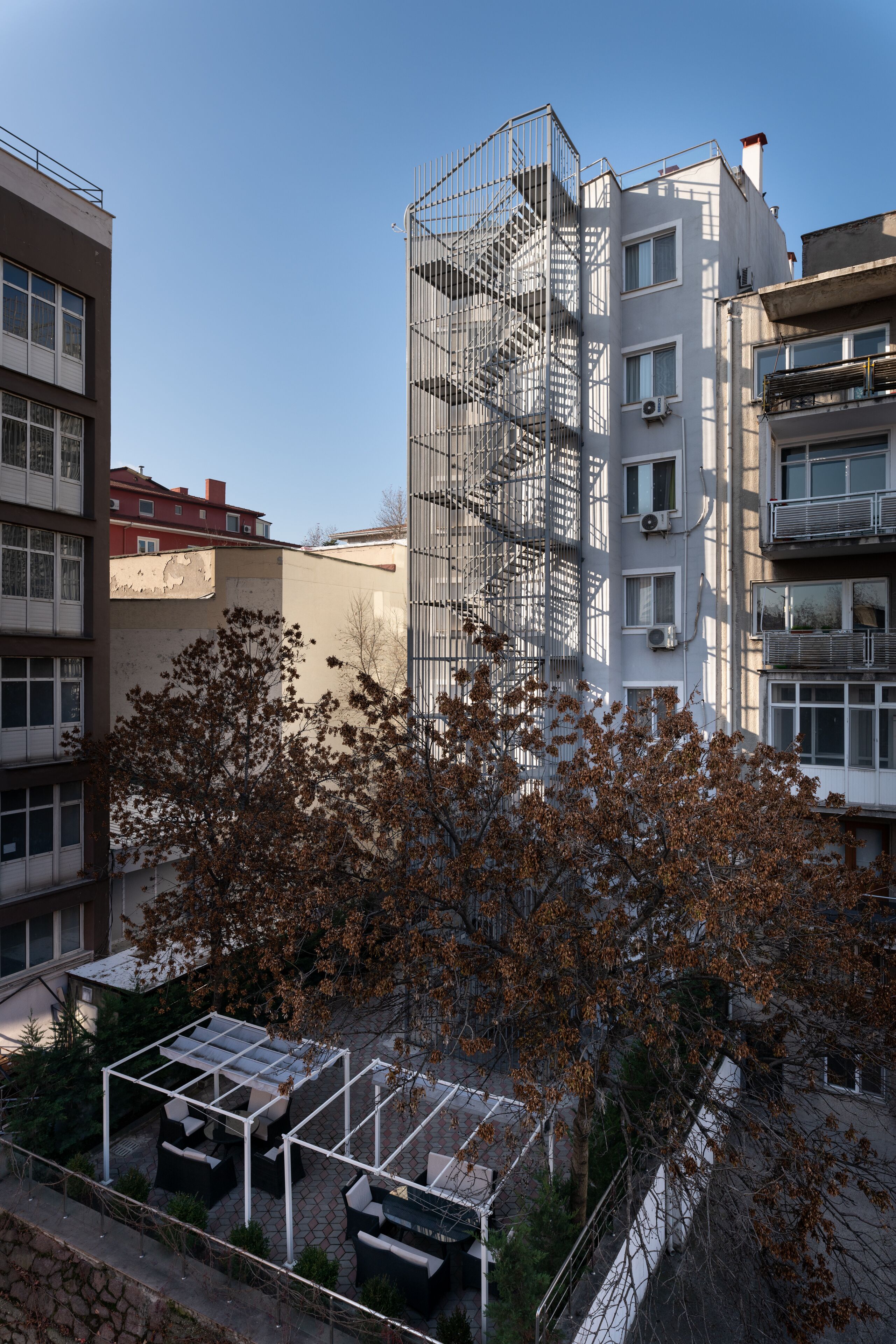 A multi-story building with a fire escape, a covered outdoor seating area, and surrounding trees.