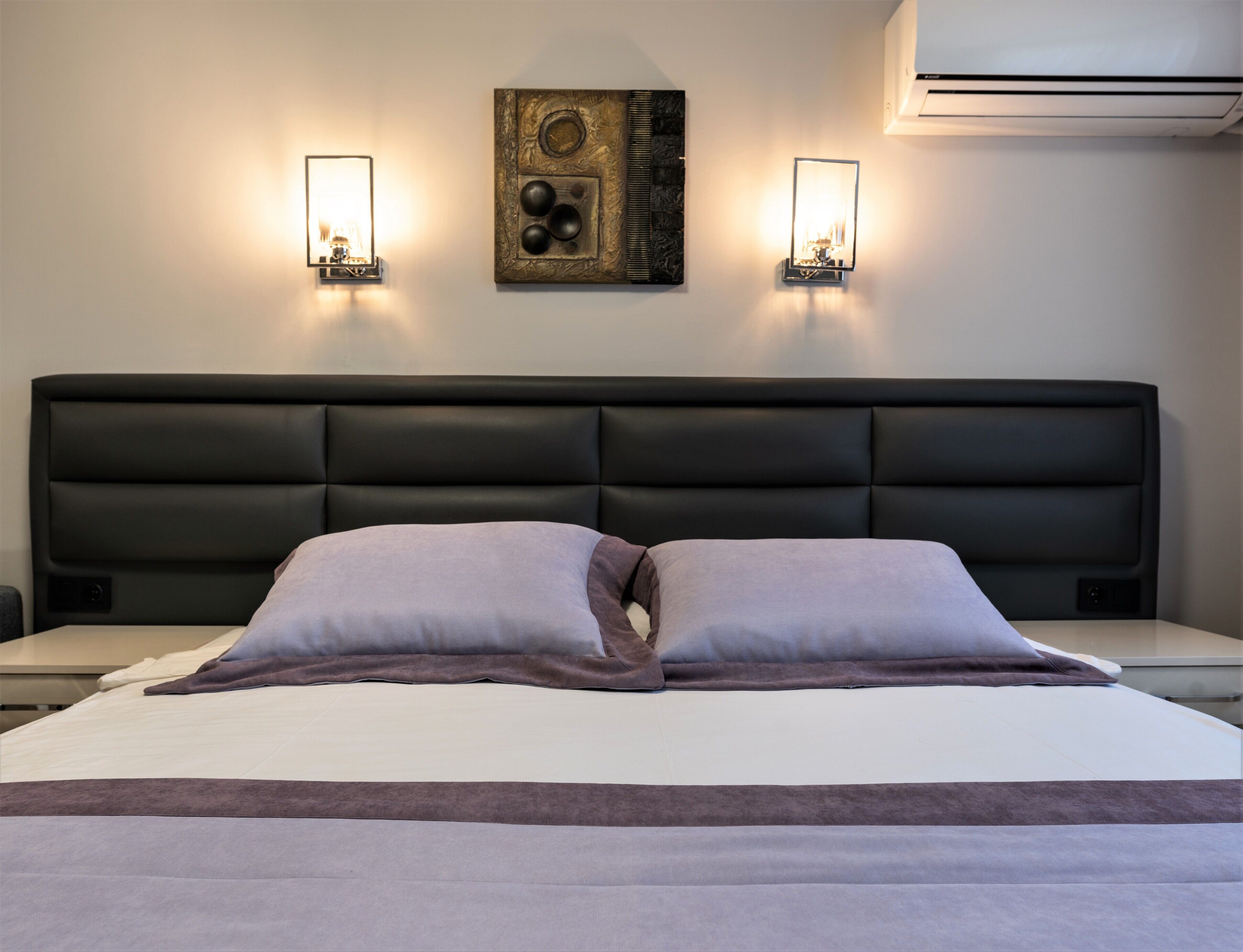 A hotel room with a large bed, two wall-mounted lights, and a decorative wall piece.