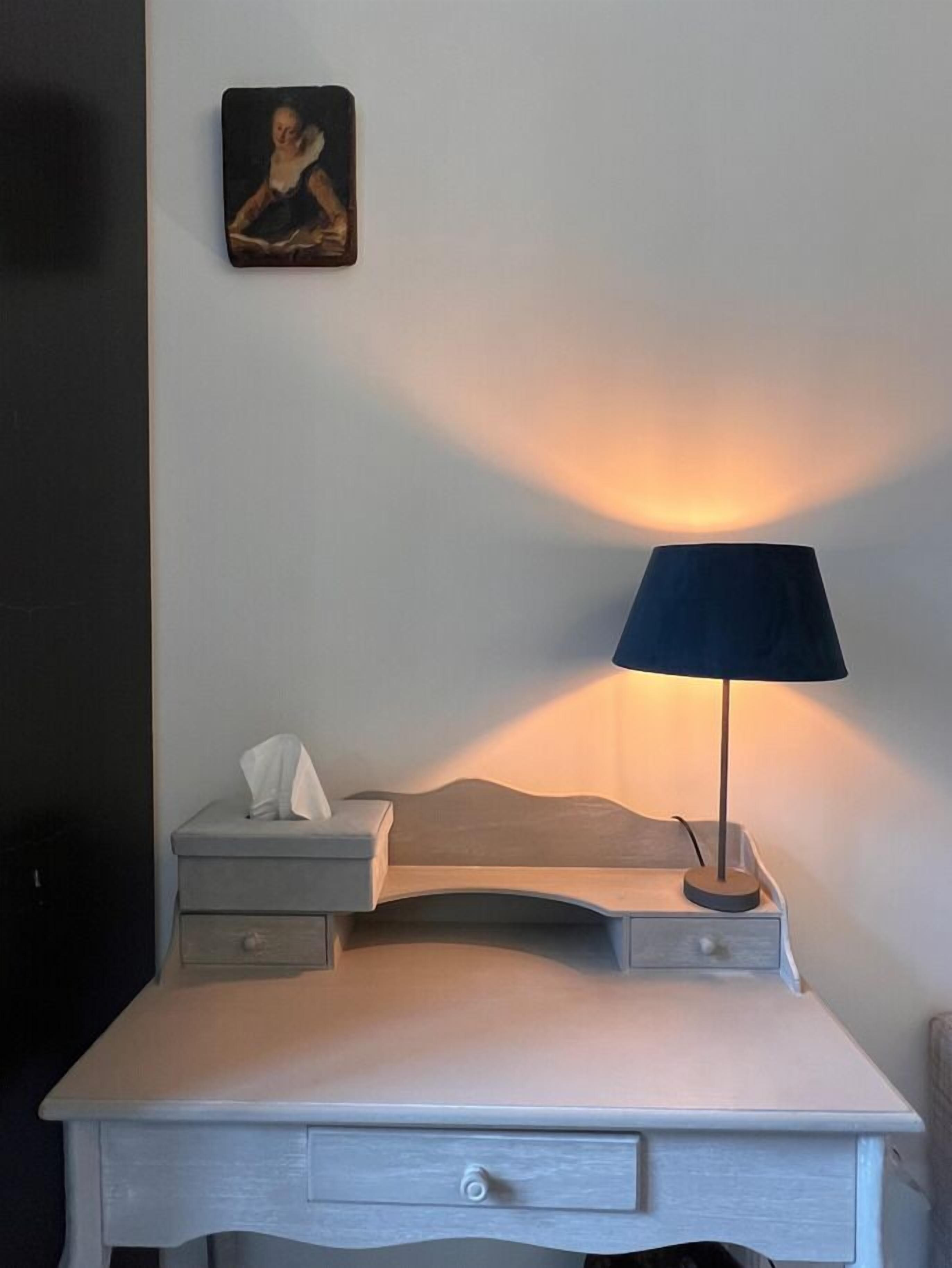 A bedside table with a lamp, a tissue box, and a small picture frame on the wall.