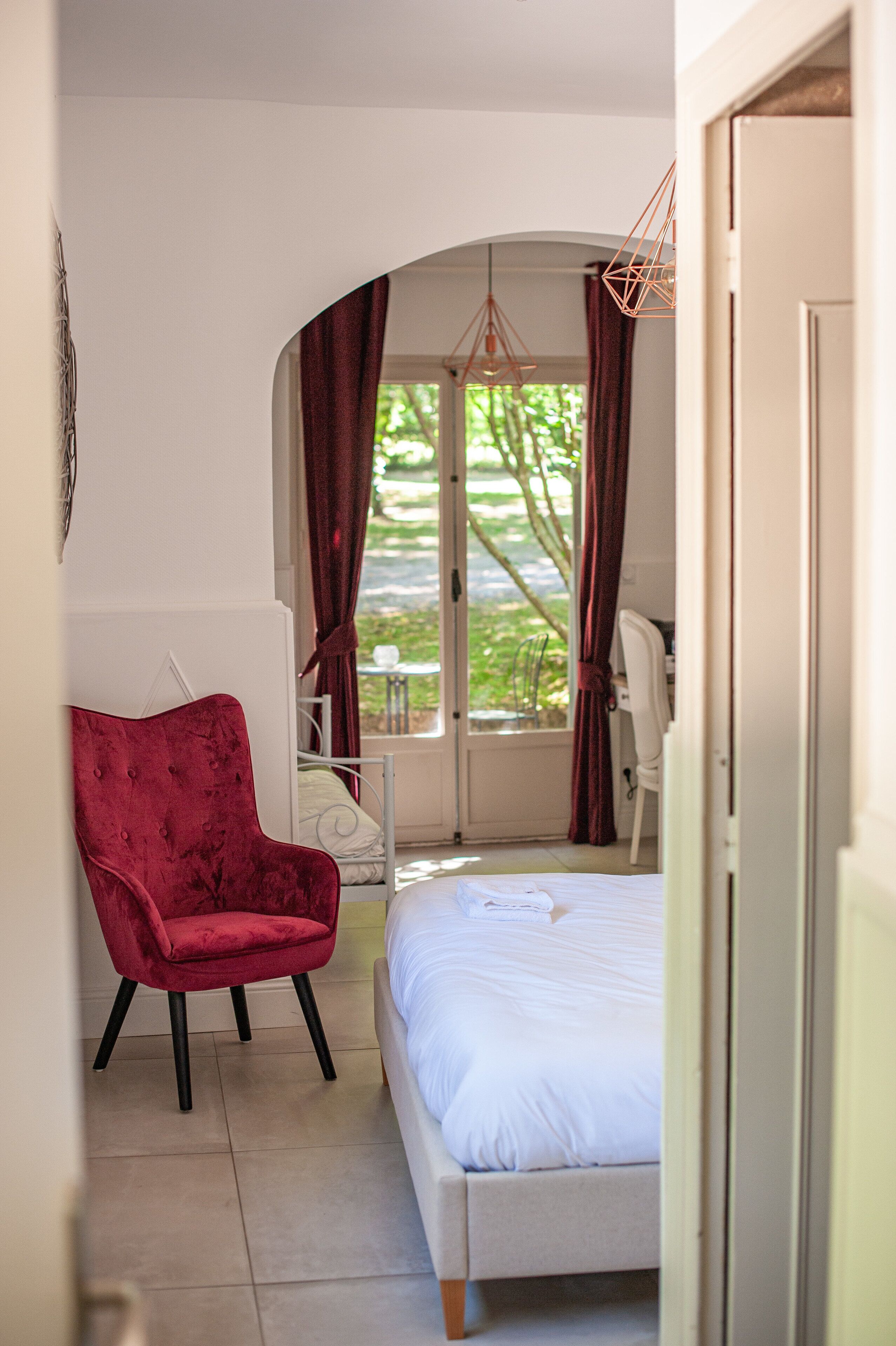 A bedroom with a bed, a red chair, a desk, and a window with curtains.