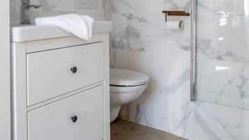 A modern bathroom with a white vanity, marble walls, a glass shower enclosure, and a toilet.