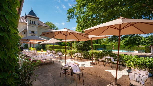 An outdoor patio with tables and chairs, umbrellas, and a pool in the background. - Château Des Ayes (Saint-Etienne-de-Saint-Geoirs)
