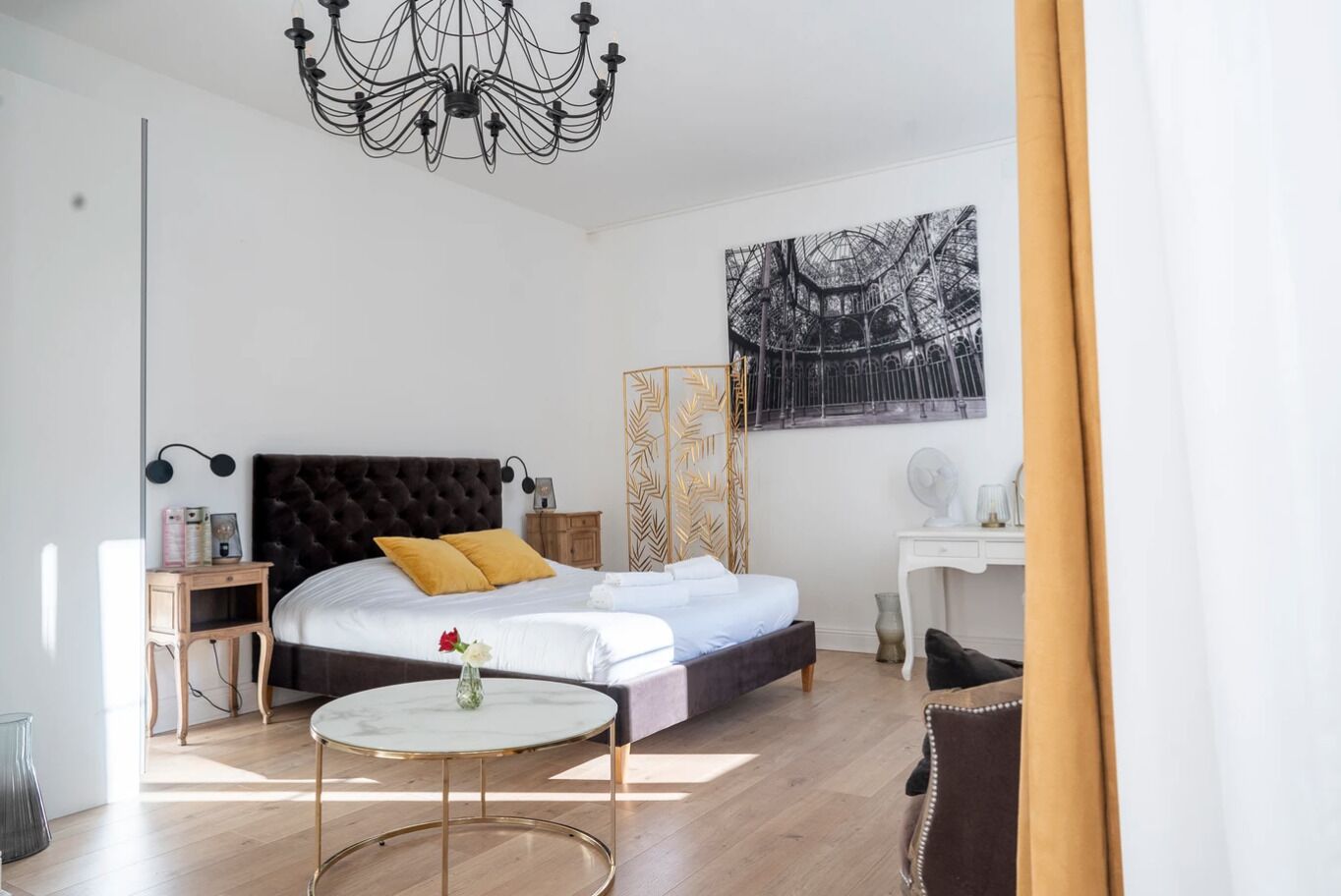 Een moderne slaapkamer met een groot bed, een rond bijzettafeltje, een bureau en een kroonluchter.