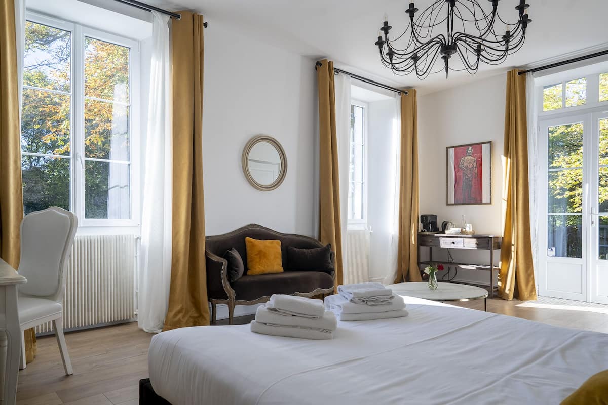 A hotel room with a bed, a desk, a chair, and a view of trees through the windows.