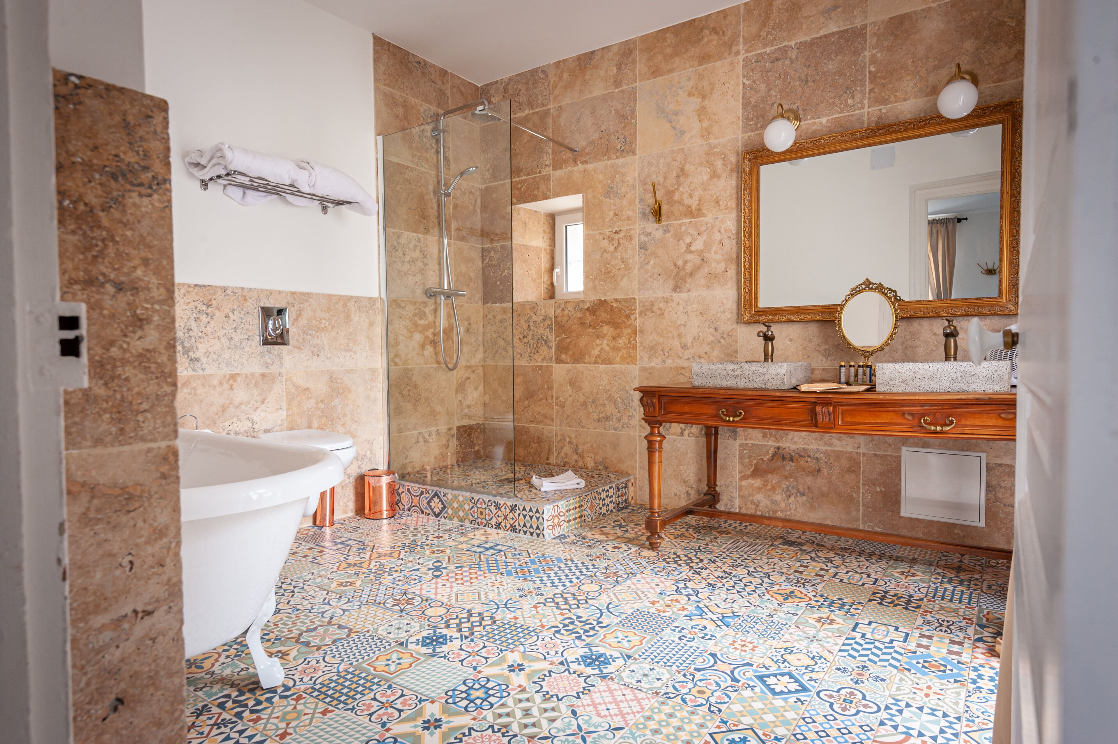 Une salle de bain avec une baignoire sur pieds, une douche à parois de verre, un meuble-lavabo en bois avec un miroir et un sol carrelé.