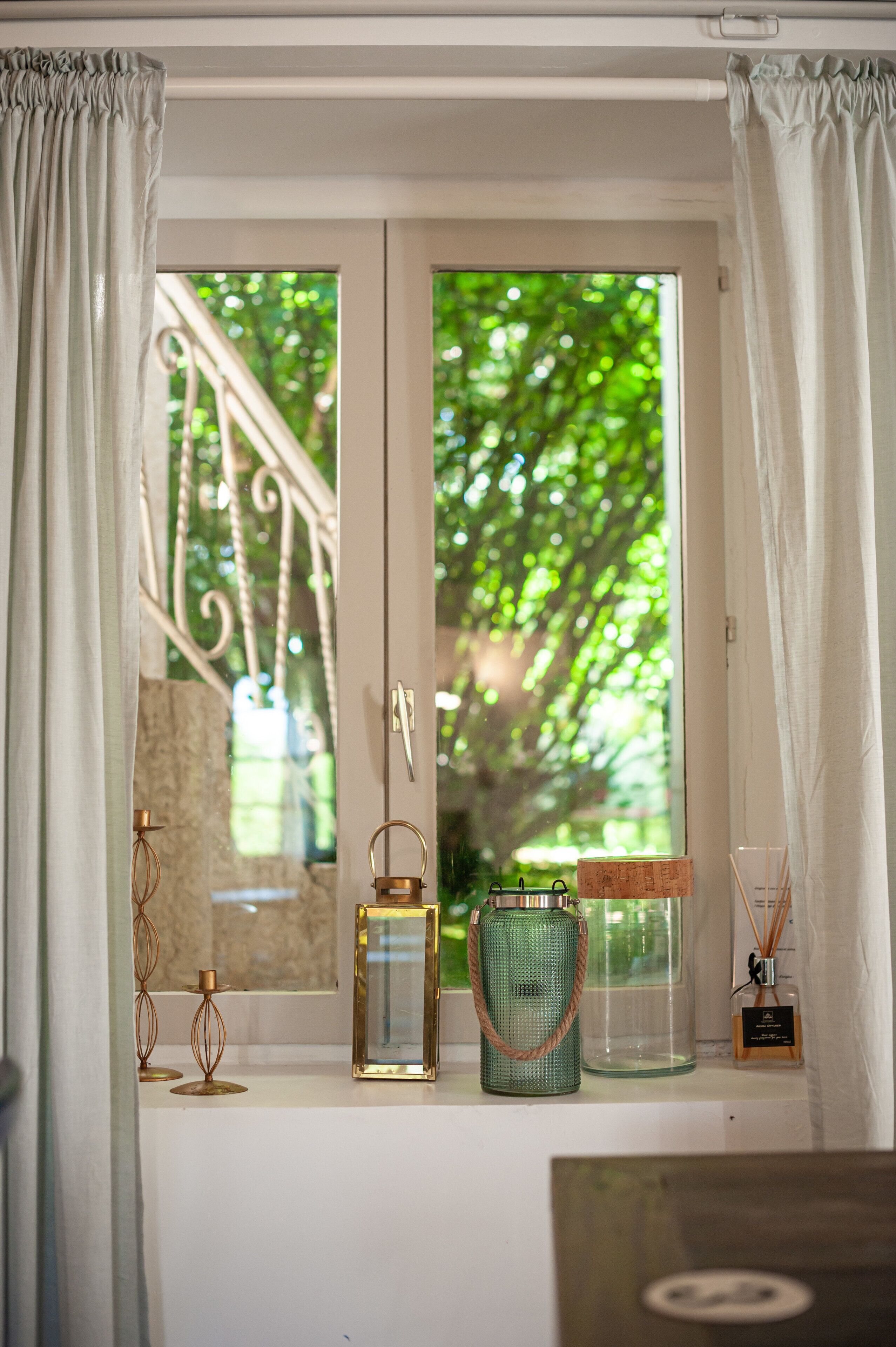 Una ventana con vistas a la vegetación, una barandilla de metal y varios objetos decorativos en el alféizar.