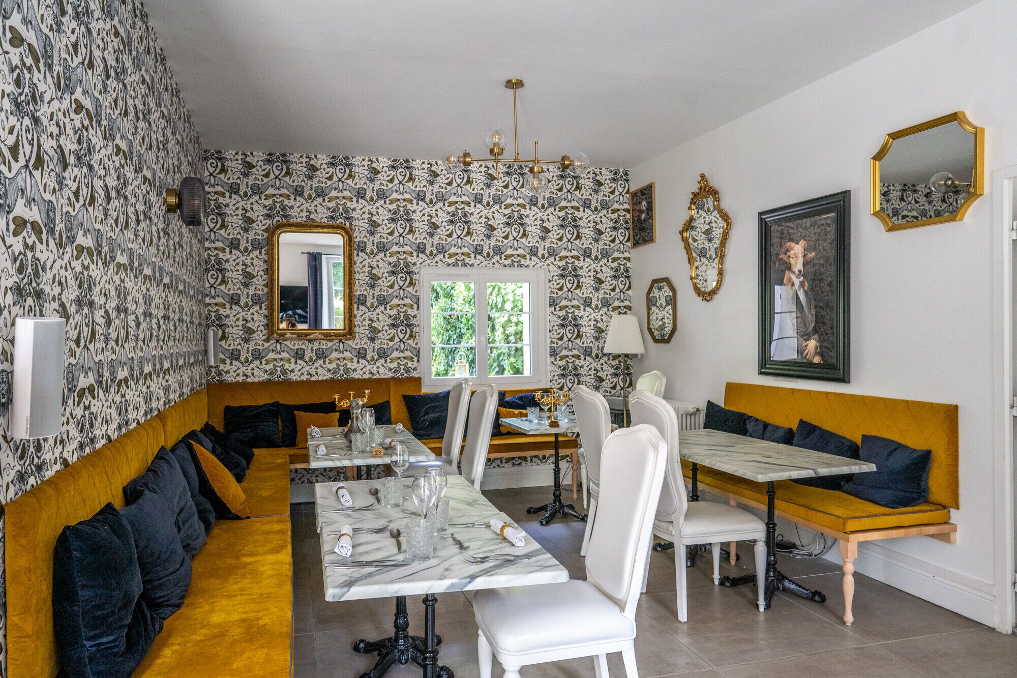 Een eetruimte met een lange tafel, witte stoelen en een geel gestoffeerde bank. Er is een raam met uitzicht op groen.