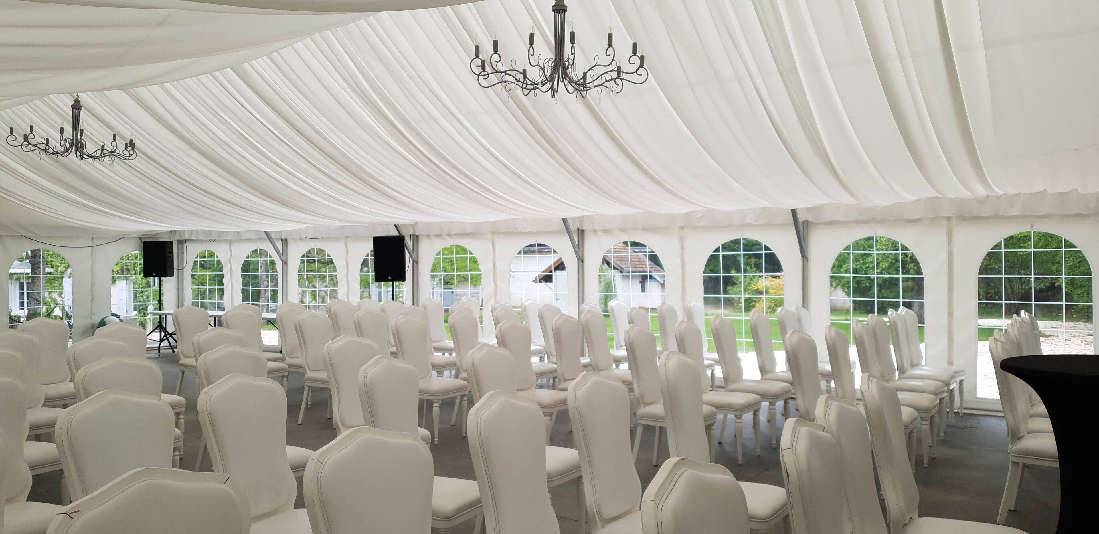 A tented event space with rows of white chairs and arched windows.