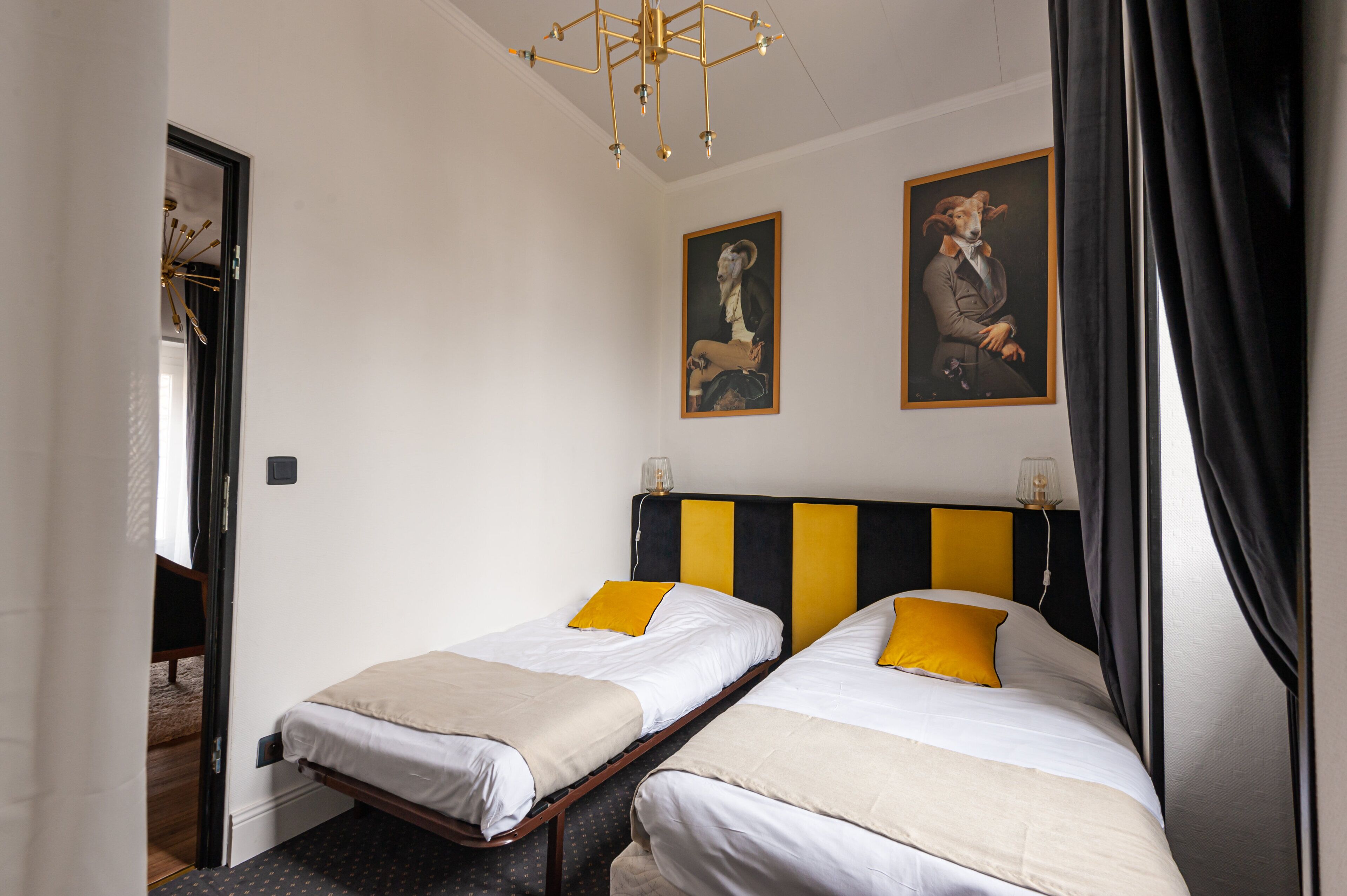 Ein Hotelzimmer mit zwei Einzelbetten, einer modernen Lüster und zwei gerahmten Portraits an der Wand.