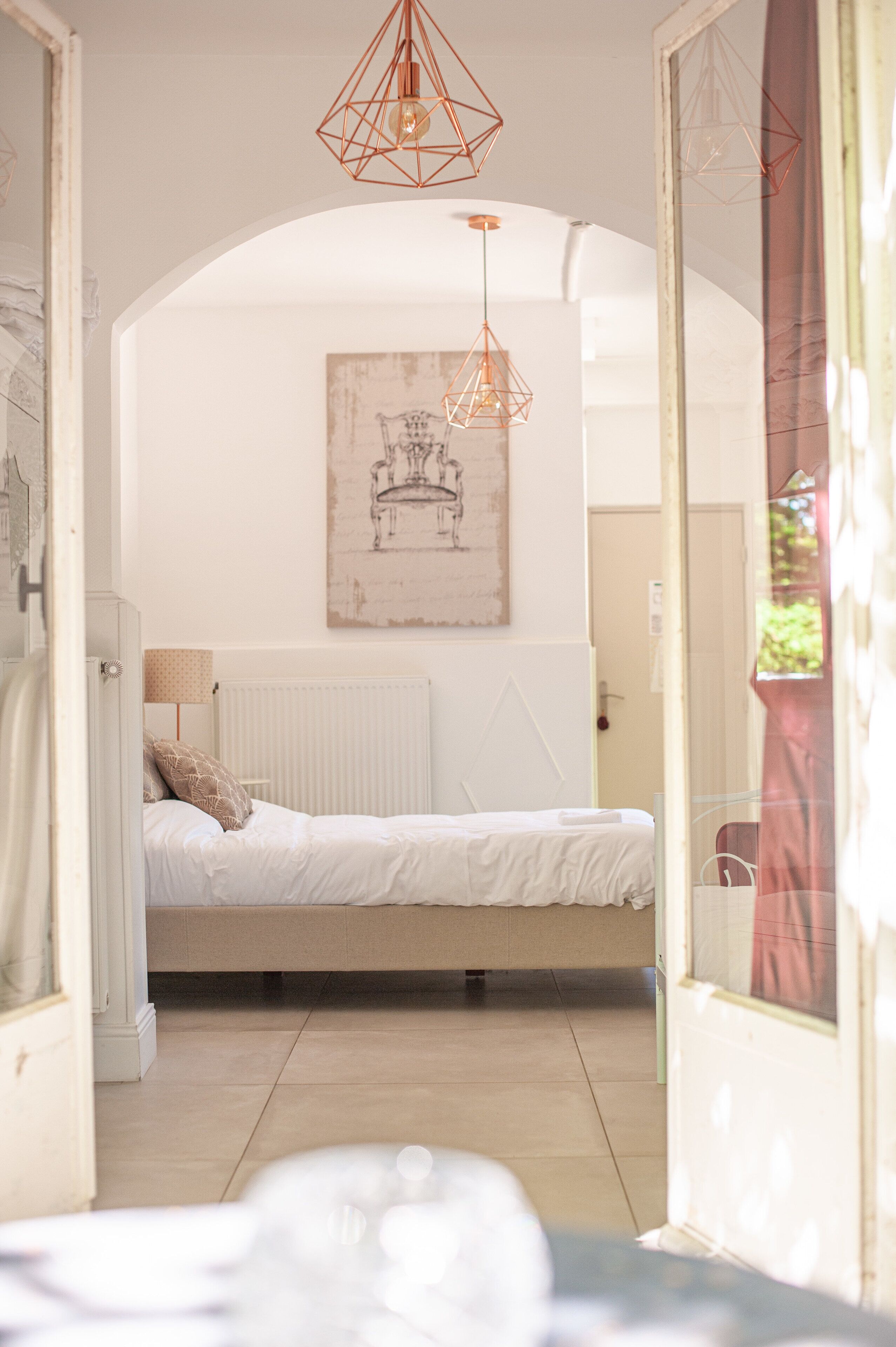 Een slaapkamer met een bed, een radiator, een hanglamp en een ingelijst schilderij aan de muur.