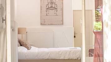A bedroom with a bed, a radiator, a hanging light fixture, and a framed picture on the wall.