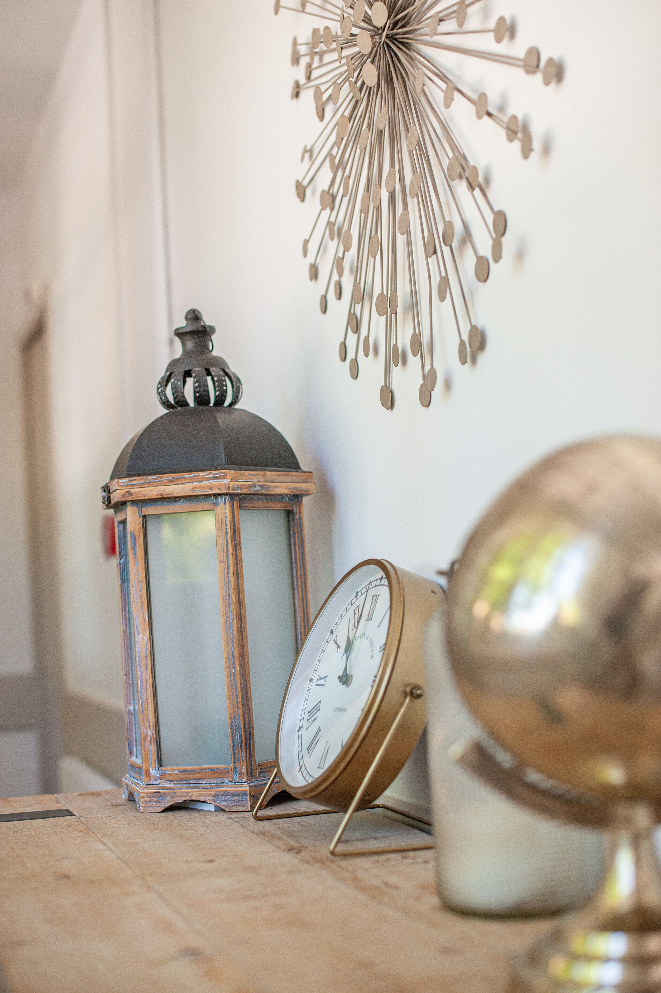 Un farolillo de estilo antiguo y un reloj de pared clásico sobre una superficie de madera.