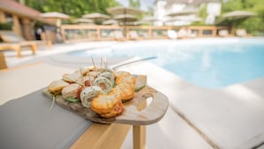 A poolside dining area with a wooden table holding a variety of sandwiches and snacks. - Château Des Ayes (Saint-Etienne-de-Saint-Geoirs)