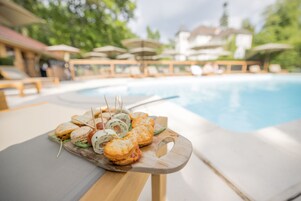 A poolside dining area with a wooden table holding a variety of sandwiches and snacks.