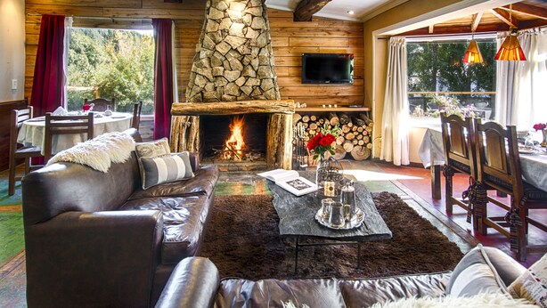 A cozy living room with a stone fireplace, leather sofas, and a dining area with a table set for two. - Equs Posada de Campo (San Carlos de Bariloche)