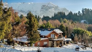 A chalet with a balcony, surrounded by snow-covered trees and mountains in the background. - Equs Posada de Campo (San Carlos de Bariloche)