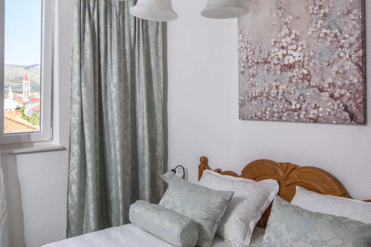 Un dormitorio con cama, cortinas, un cuadro y una araña.