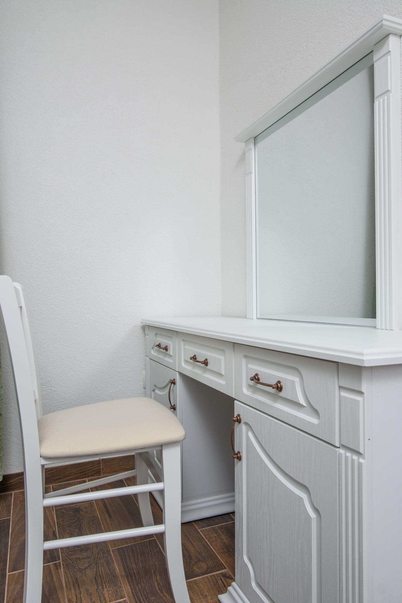 A white vanity with a mirror, a chair, and a cabinet.