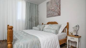 Un dormitorio con una cama de madera, ropa de cama blanca, una mesita de noche con una lámpara y un cuadro floral en la pared.