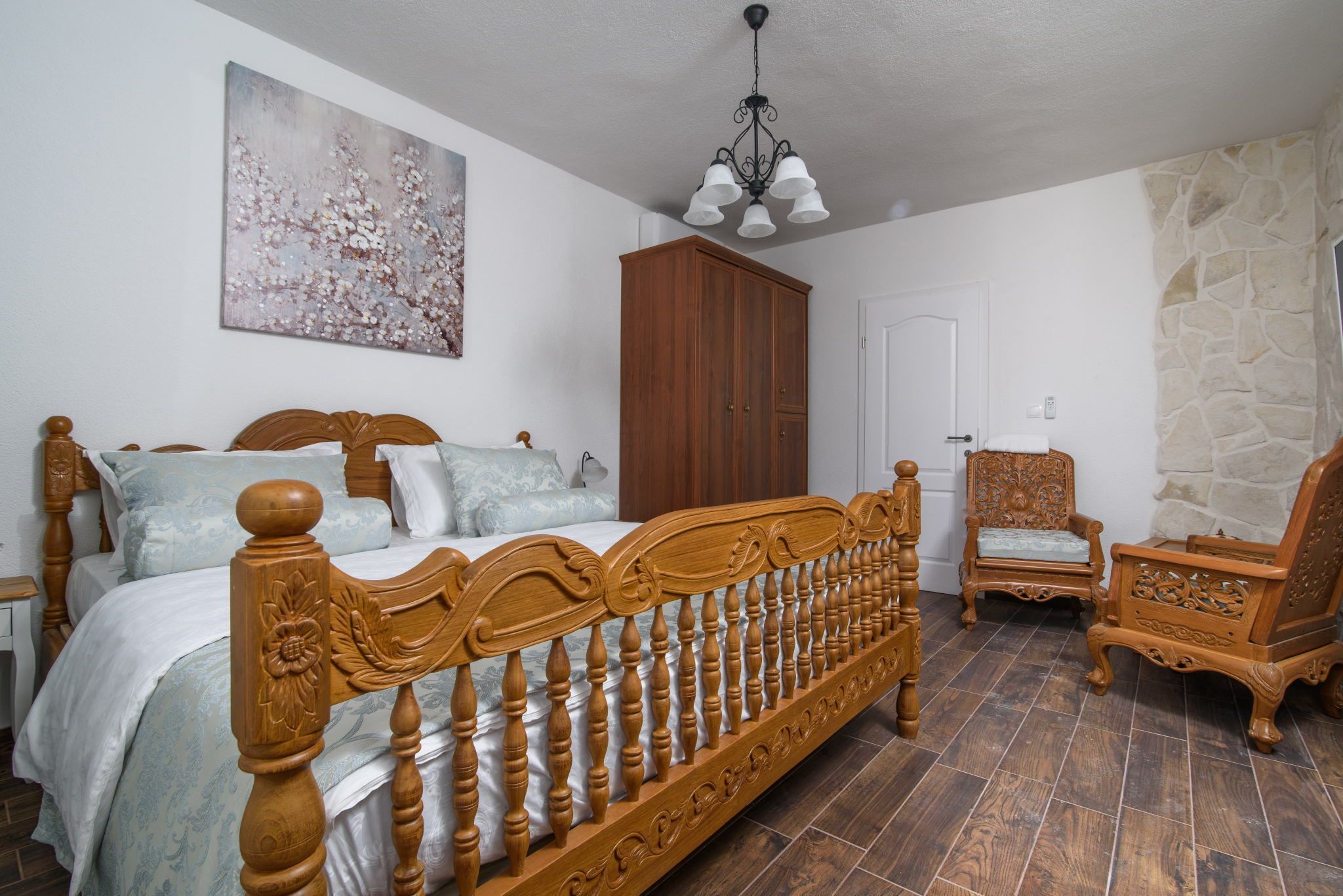 A bedroom with a wooden bed, a wardrobe, a chair, and a painting on the wall.