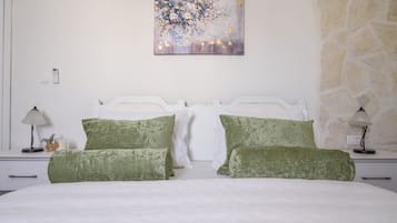 A bedroom with a white bed, green pillows, a painting on the wall, and a stone wall.