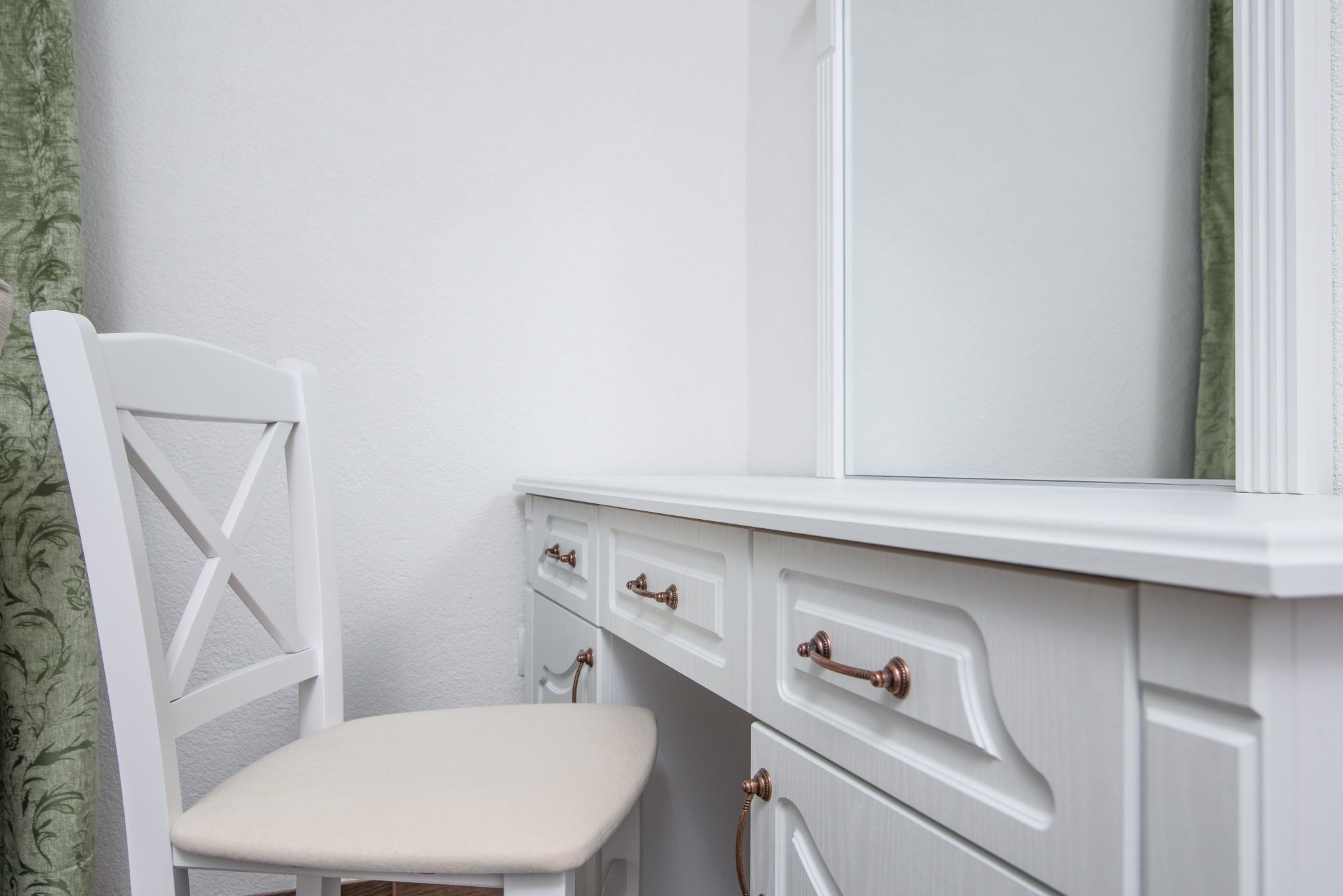 A white vanity with a mirror, a chair, and two drawers with brass handles.