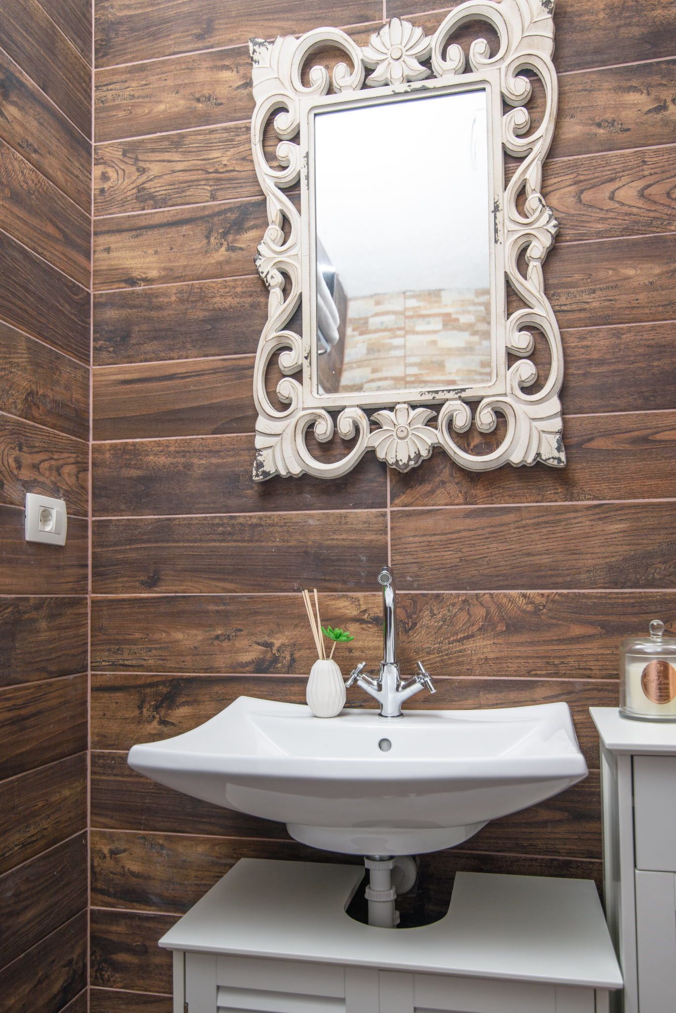 Un baño con pared de madera, un lavamanos blanco y un espejo decorativo.