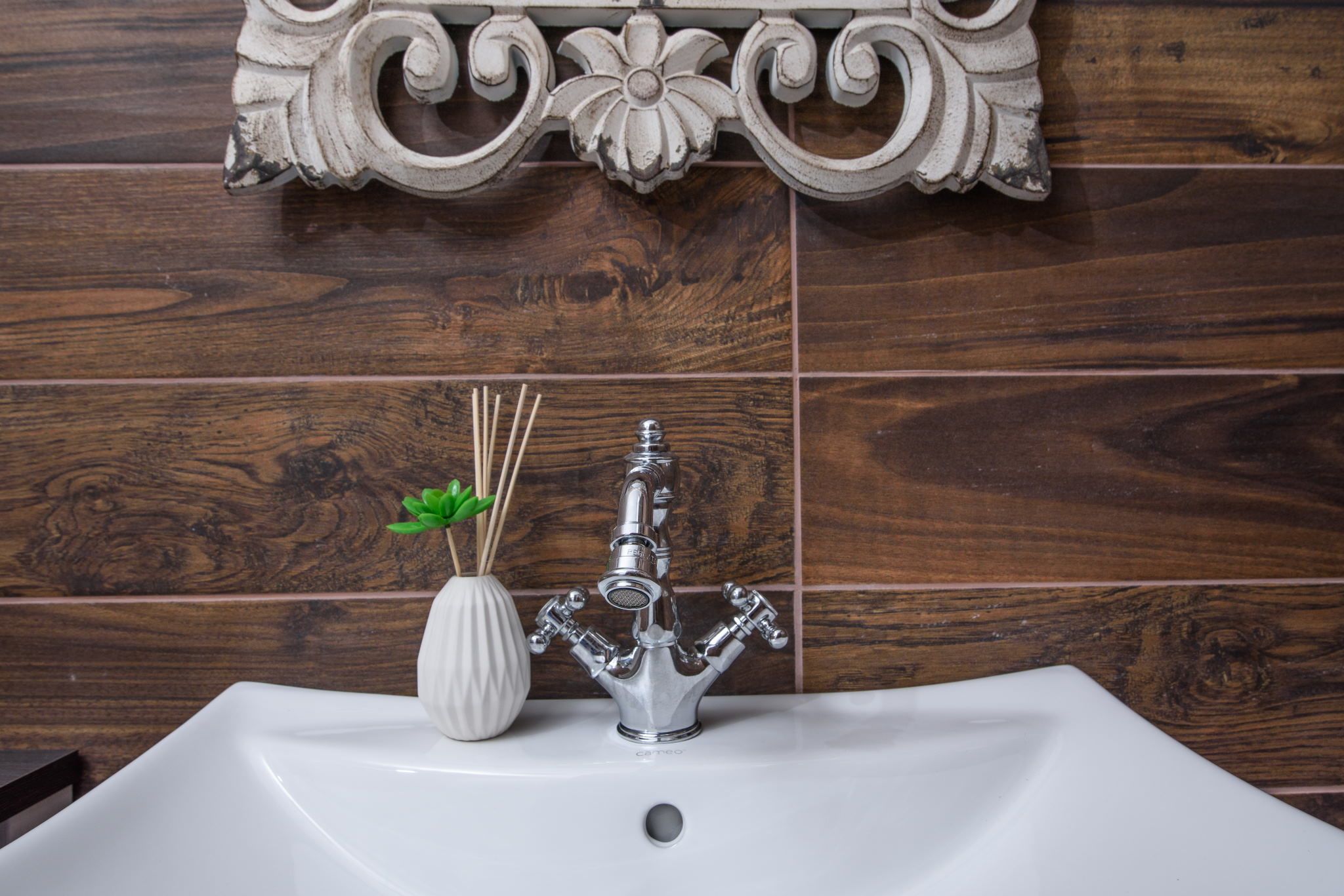 A bathroom with a white sink, a decorative wall panel, and a white vase with a plant.