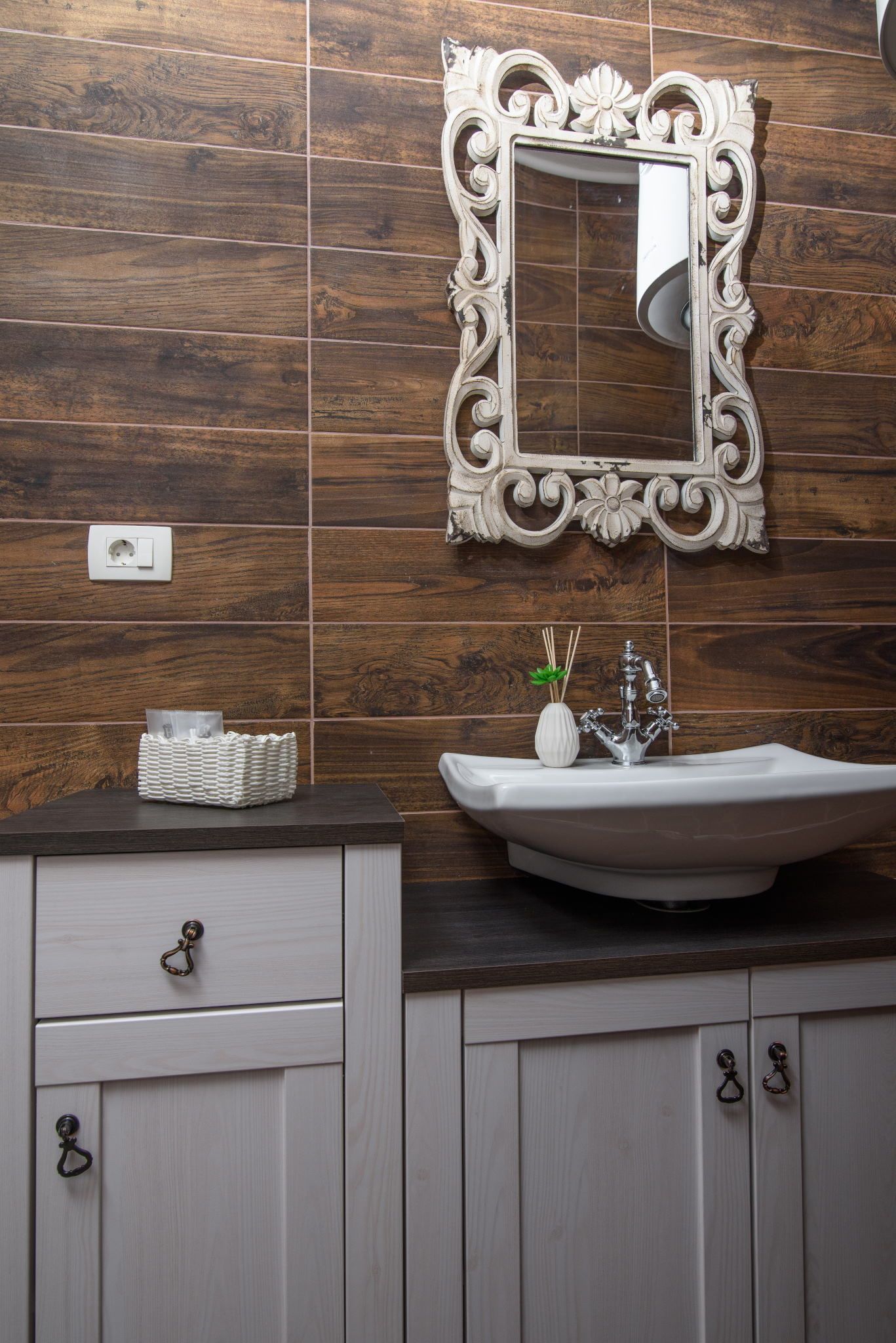 Une salle de bain avec un mur en bois, un lavabo blanc agrémenté d’un miroir décoratif et un meuble blanc avec des tiroirs.