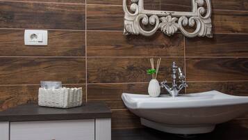 Une salle de bain avec un mur en bois, un lavabo blanc agrémenté d’un miroir décoratif et un meuble blanc avec des tiroirs.