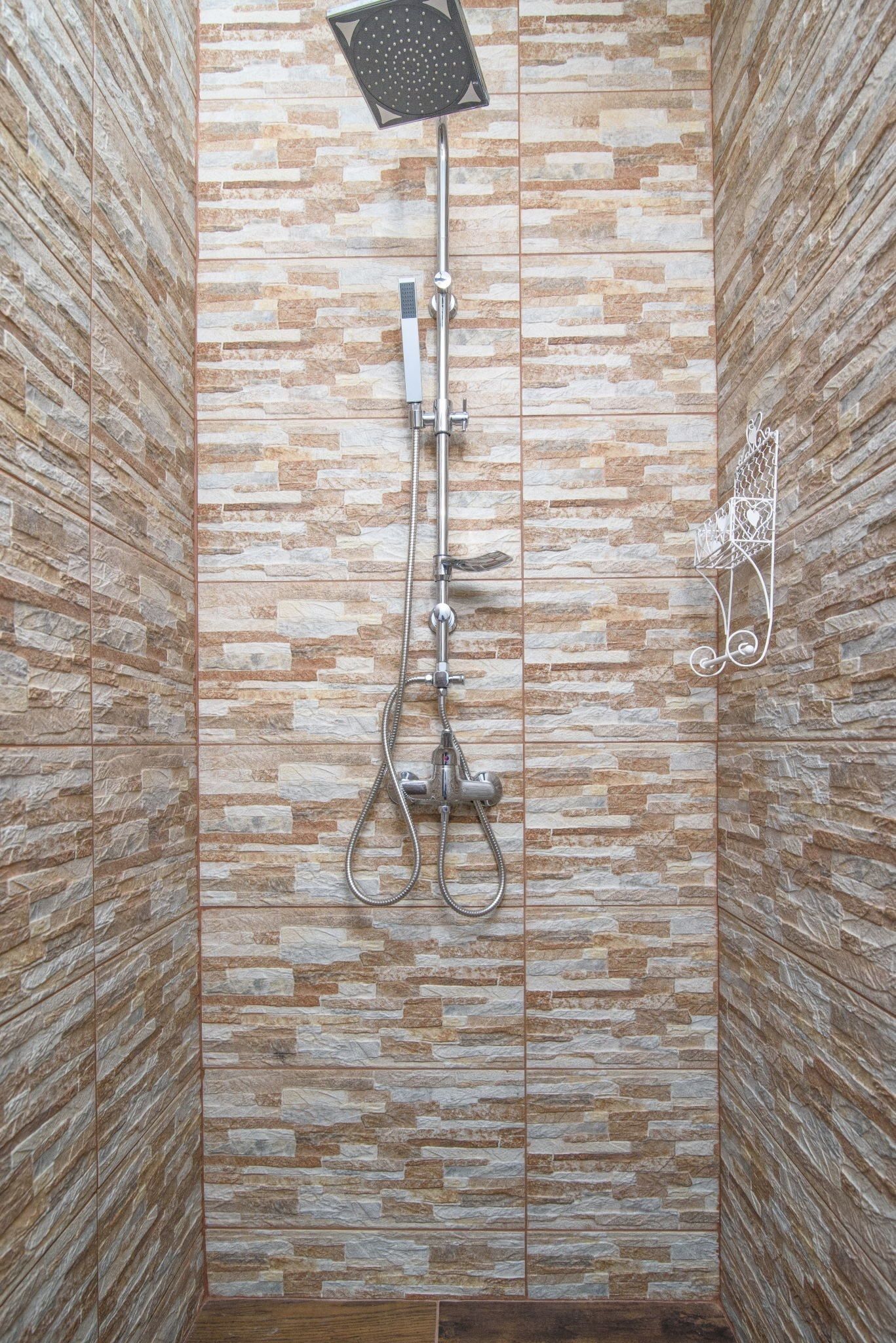 A shower with a stone-patterned wall and a metal showerhead.