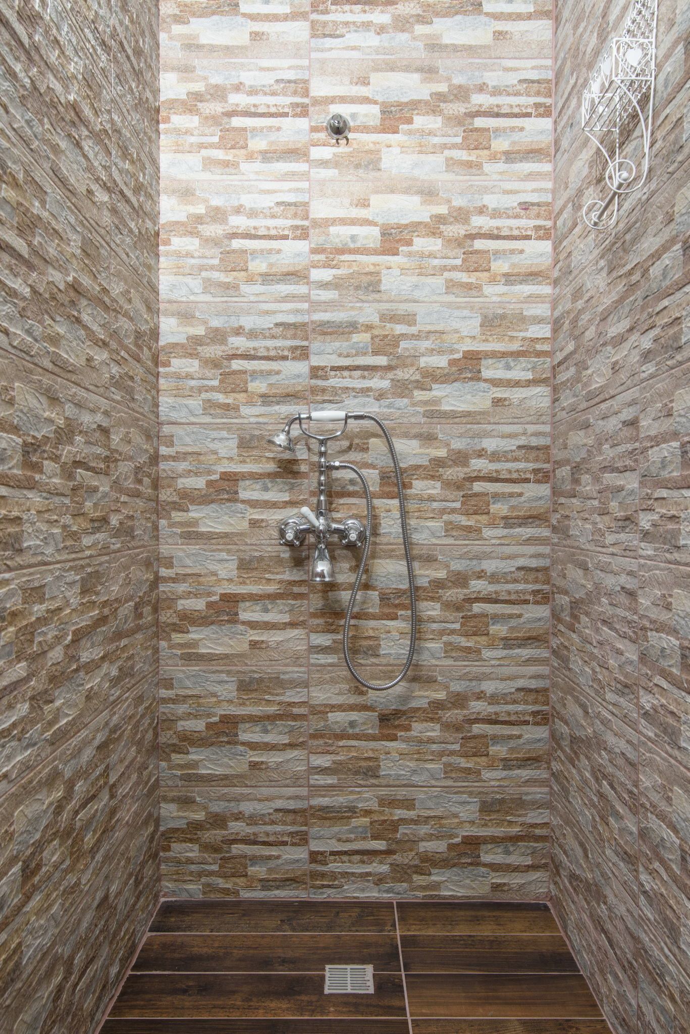 A shower with a stone tile wall and a metal showerhead.
