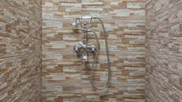 A shower with a stone tile wall and a metal showerhead.