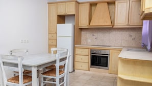 A kitchen with wooden cabinets, a white refrigerator, a stove, and a dining table with chairs. - Depis Apartments 2 (Naxos)