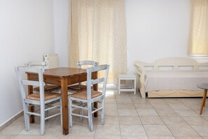 A room with a wooden dining table, two chairs, a small bedside table, and a bed with a white headboard. - Depis Apartments 2 (Naxos)
