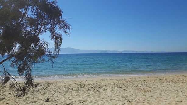 A beach with clear blue water, sandy shore, and distant mountains. - Depis Sea Side Villas (Naxos)