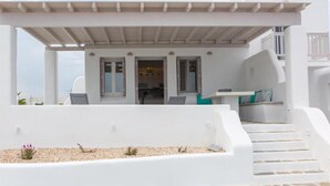 A white building with a covered outdoor seating area, a staircase, and a view of the sea. - Depis Sea Side Villas (Naxos)