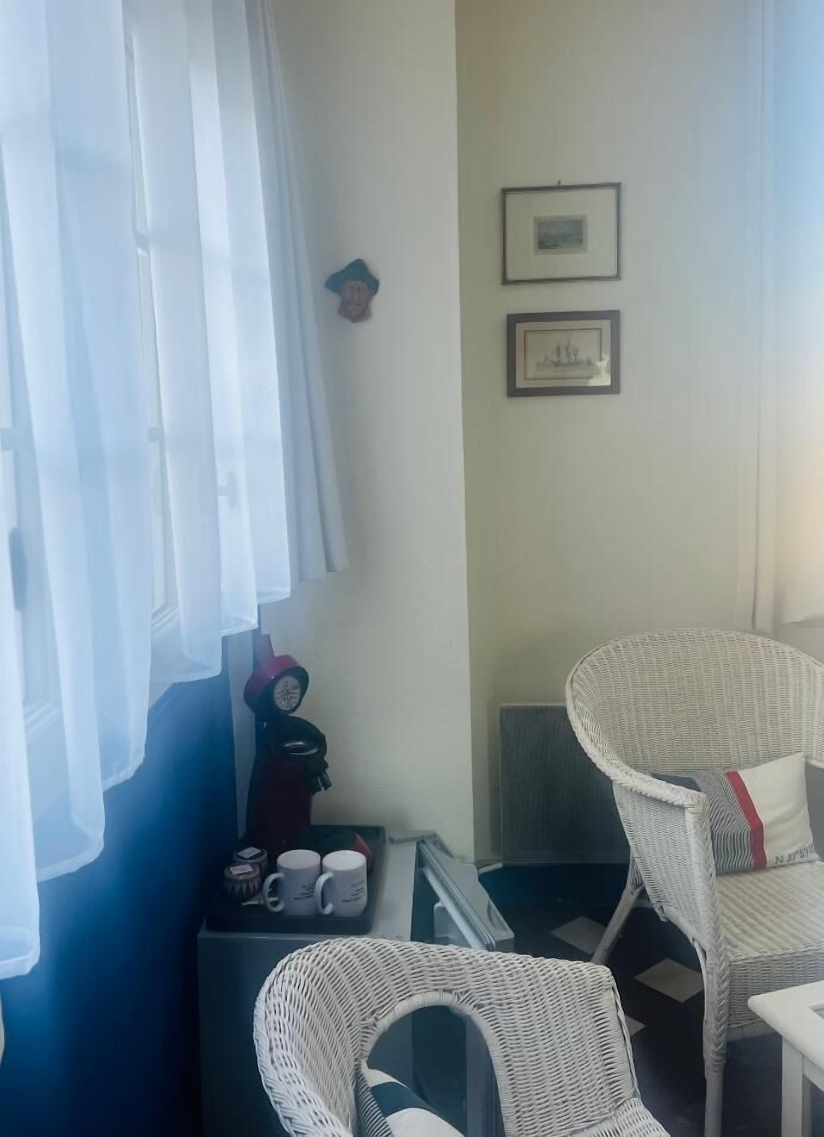 A room with two wicker chairs, a small table with mugs, and a wall-mounted picture frame.