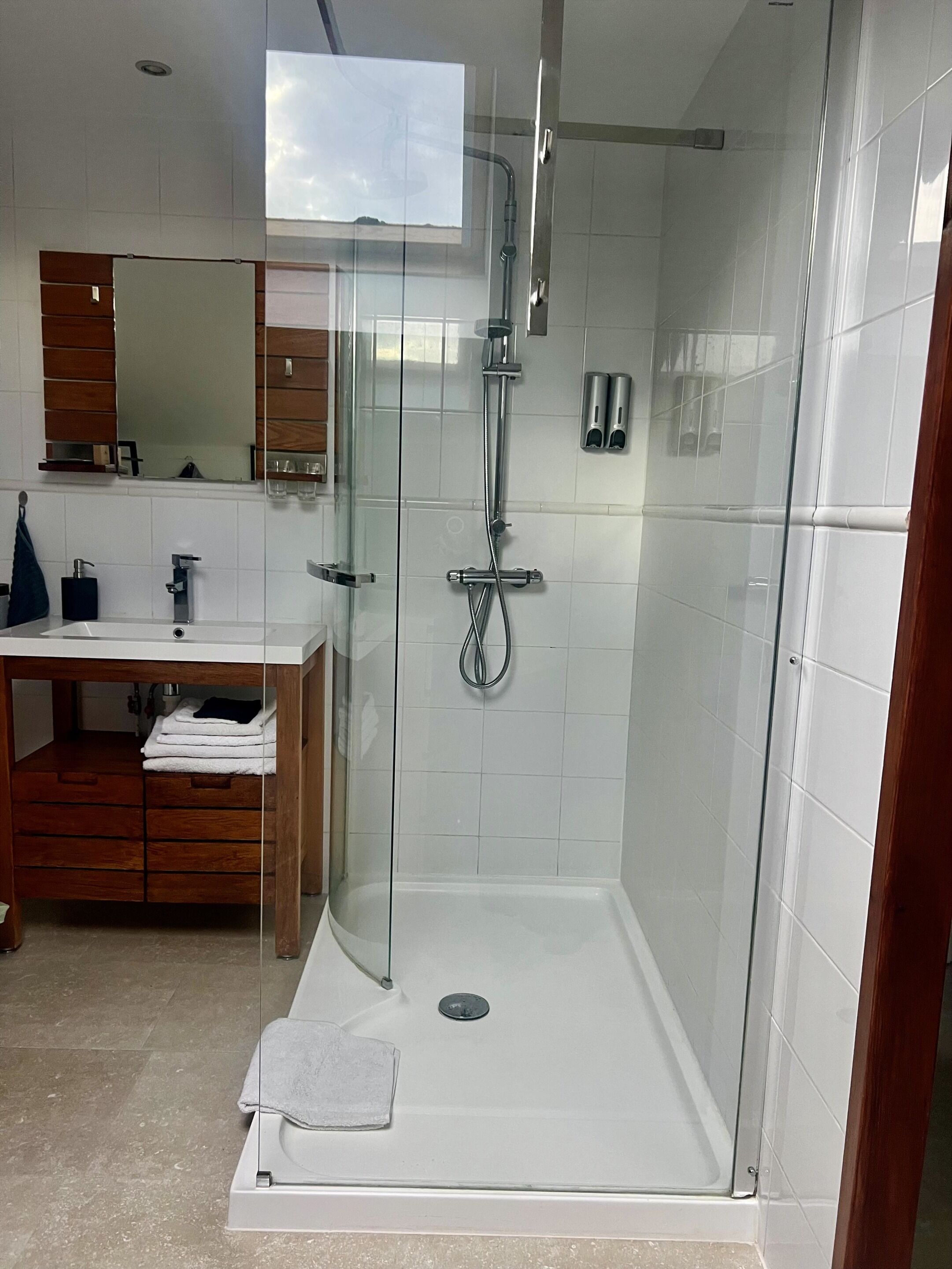 Un baño moderno con ducha envuelta en vidrio, tocador de madera y un espejo grande.
