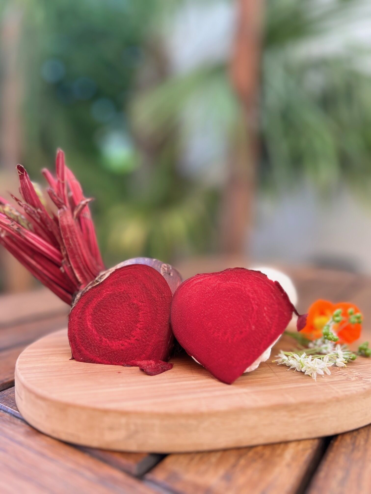 A wooden table with a beetroot cut in half and a bunch of red flowers.