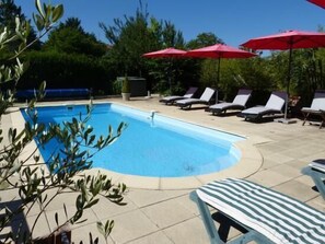 Una piscina con sillas de descanso y sombrillas rojas.