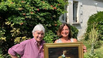 Two individuals holding a framed artwork in front of a building with a sign that reads 'Les Tuileries de Chanteloup.'