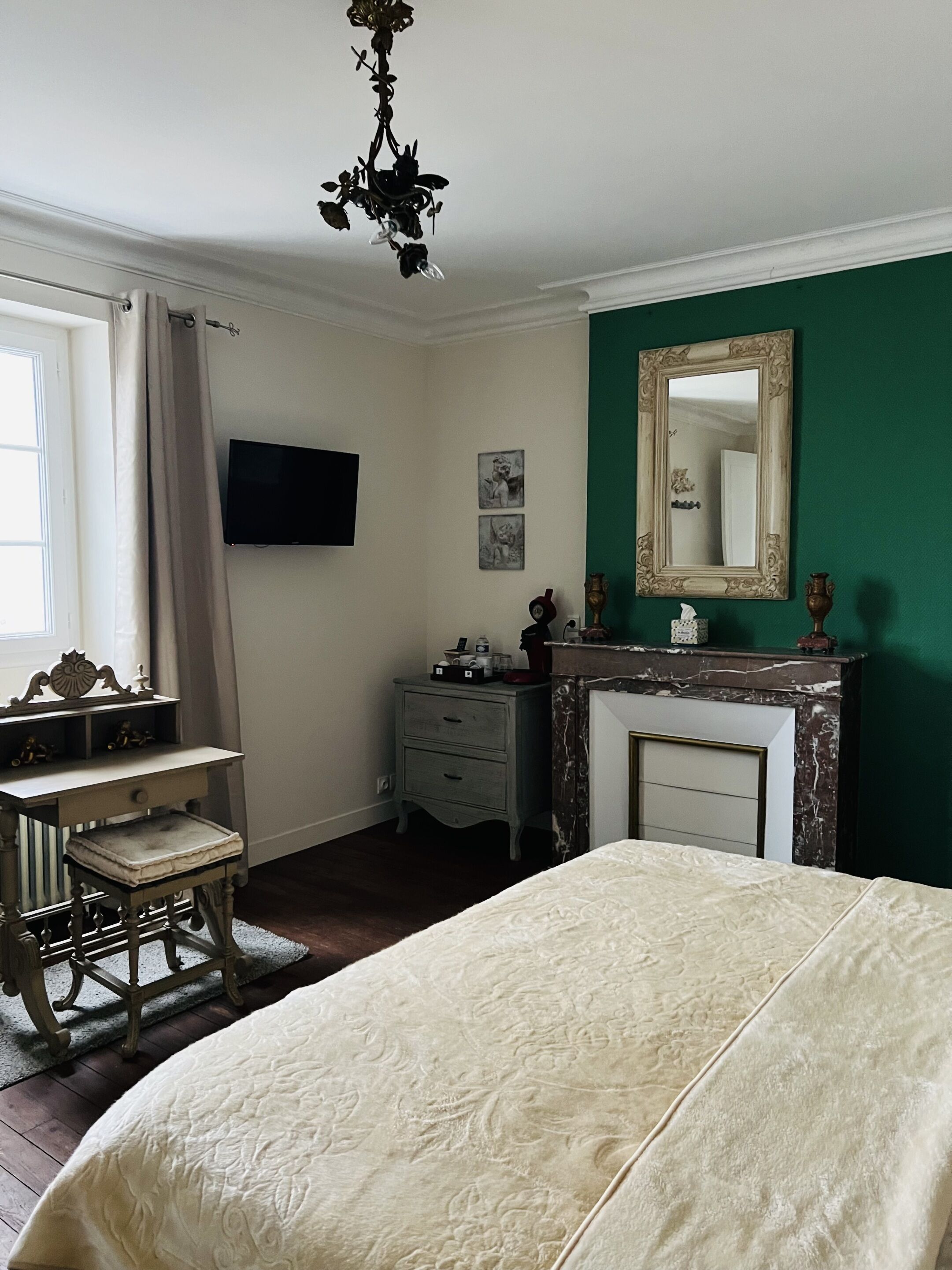 A bedroom with a bed, dresser, vanity, and a fireplace.