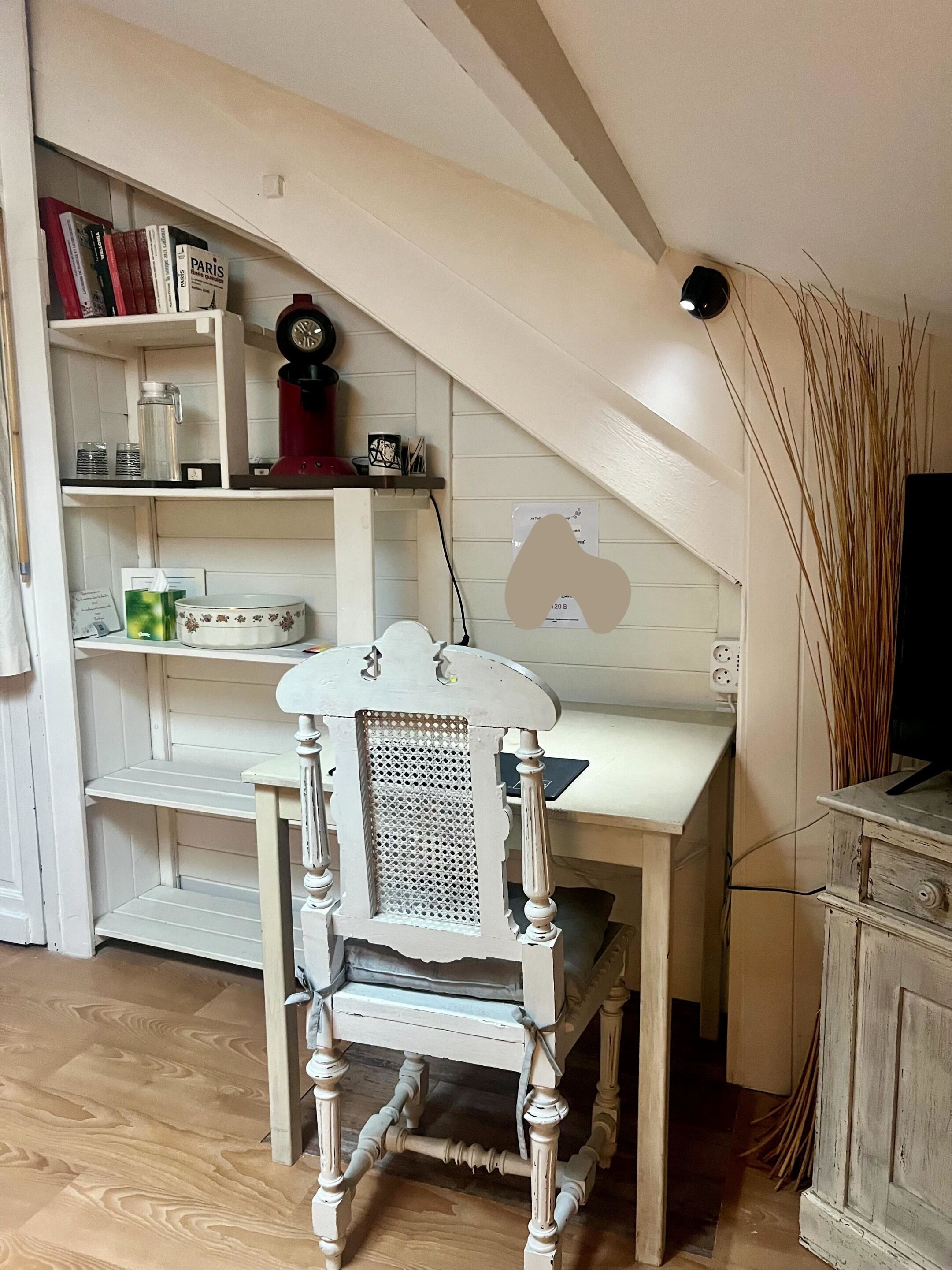 A room with a white desk, a white chair, a bookshelf with books and decorative items, and a television on a wooden cabinet.