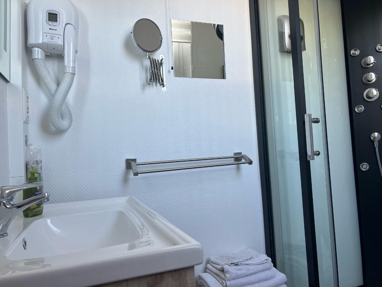 A bathroom with a white sink, a hairdryer, a mirror, and a towel rack.