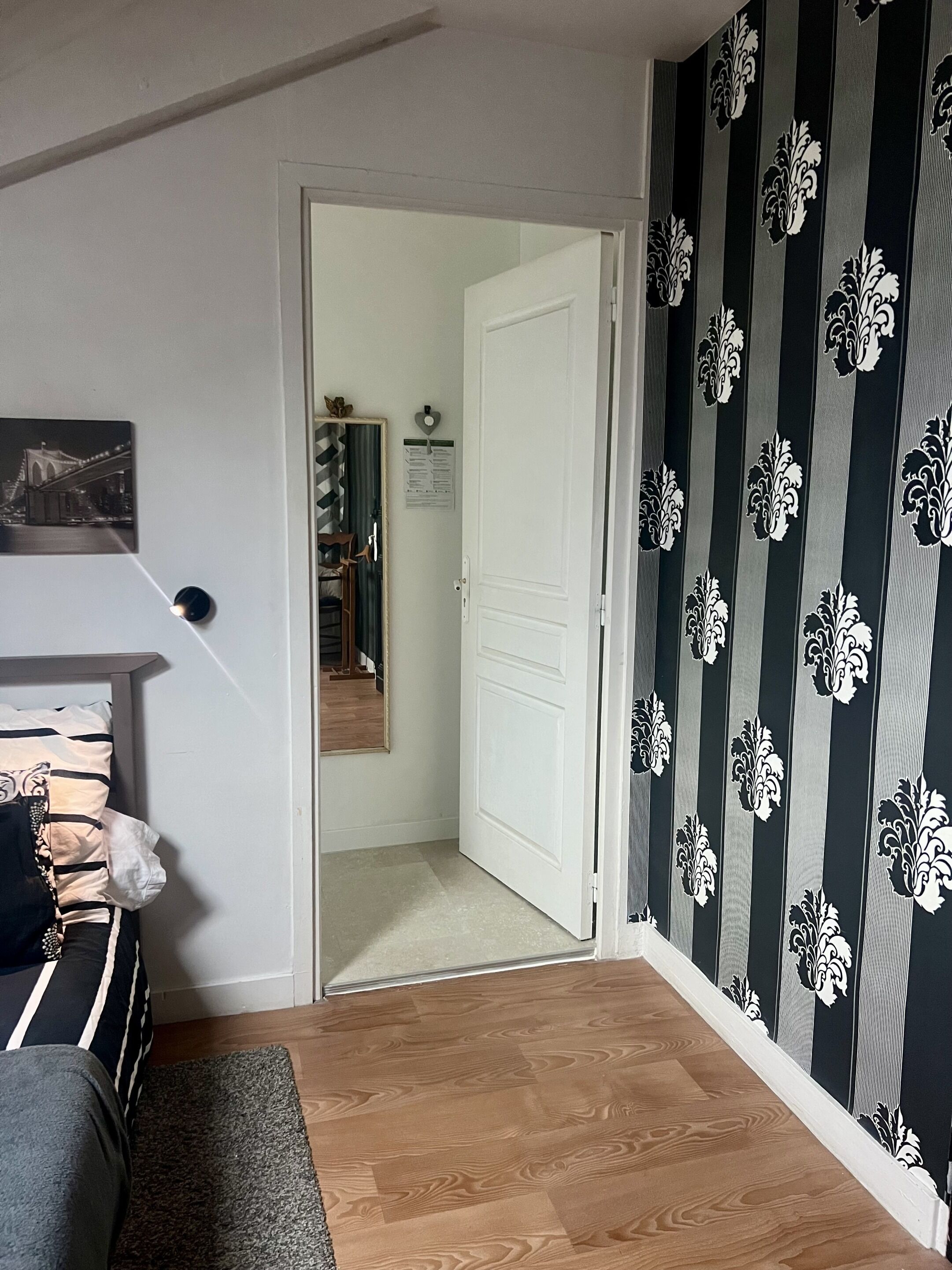 Un pasillo con suelo de madera, una puerta blanca, un espejo y un papel tapiz decorado.