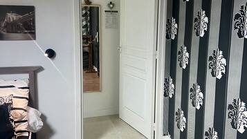 Un pasillo con suelo de madera, una puerta blanca, un espejo y un papel tapiz decorado.