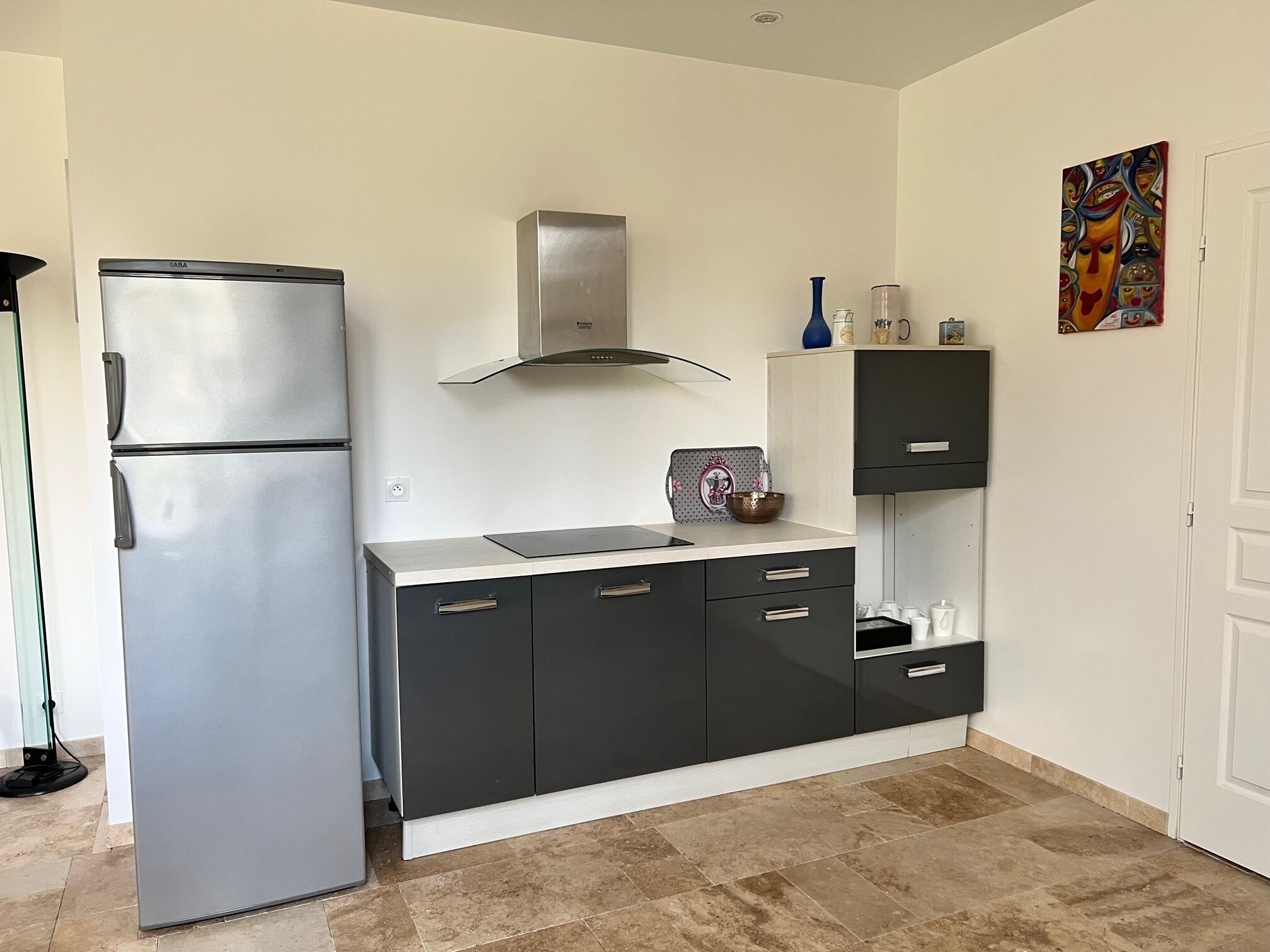 Uma cozinha compacta com geladeira de aço inoxidável, fogão moderno e armário com gavetas.